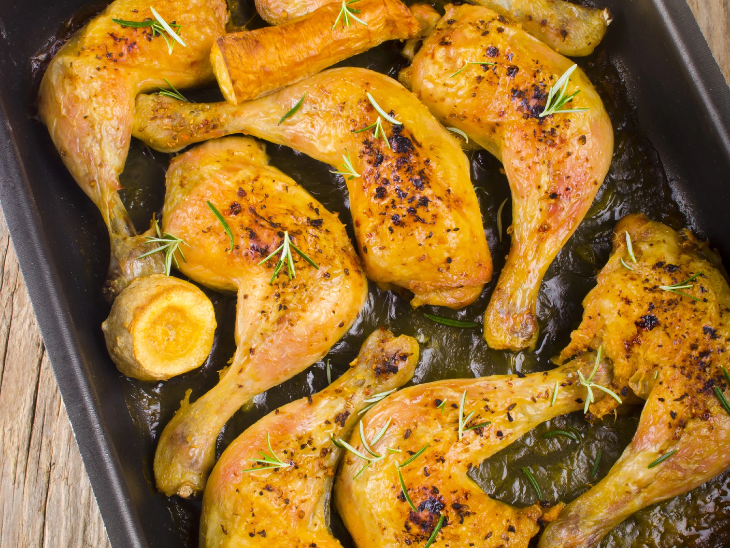 marinated chicken drumsticks in a baking tray with herbs sprinkled on top.